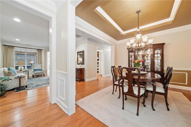 dining area with crown molding, a chandelier, light wood finished floors, and wainscoting