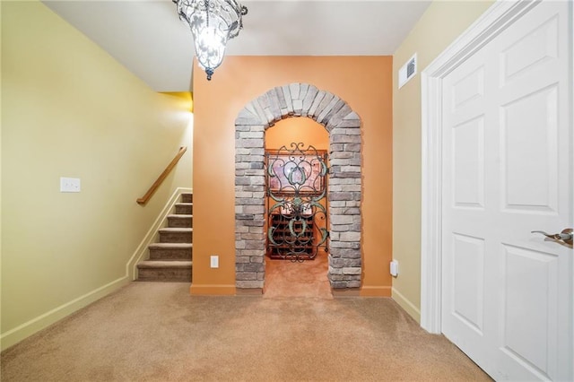 carpeted entrance foyer featuring baseboards, arched walkways, and stairs