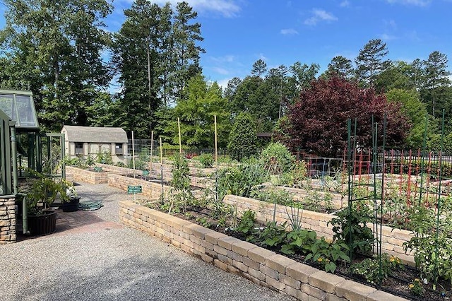 view of yard with a vegetable garden, fence, an outdoor structure, and view of wooded area
