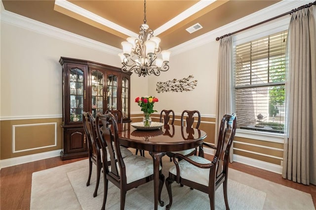 dining room with wood finished floors, a raised ceiling, a chandelier, crown molding, and plenty of natural light