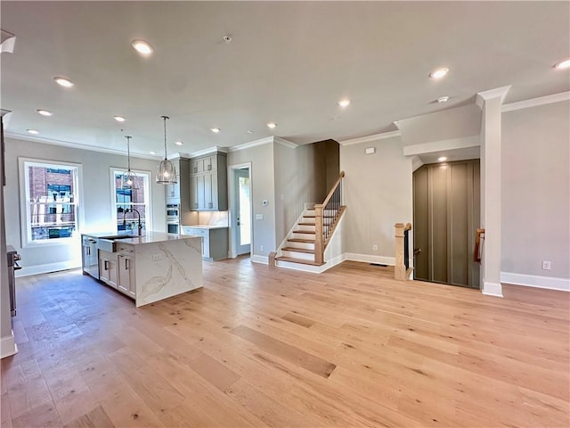 kitchen with light stone counters, decorative light fixtures, a center island with sink, light hardwood / wood-style flooring, and crown molding