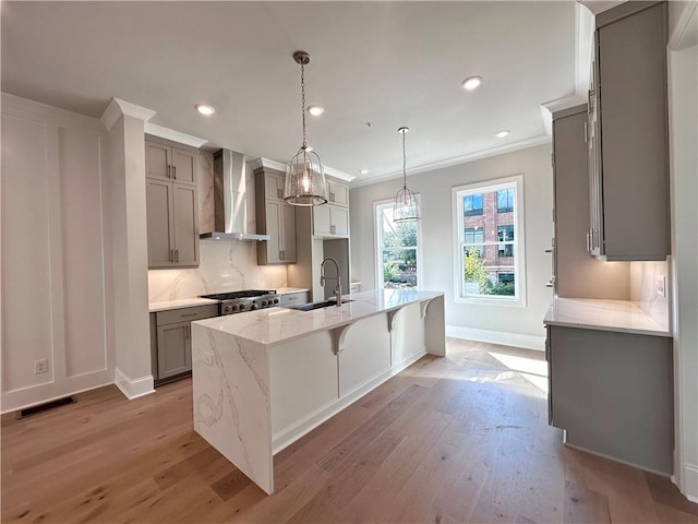 kitchen with wall chimney exhaust hood, visible vents, a sink, light wood finished floors, and gray cabinetry