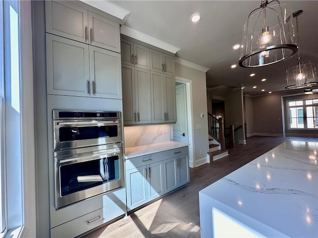 kitchen with ornamental molding, light stone counters, gray cabinets, double oven, and wood finished floors