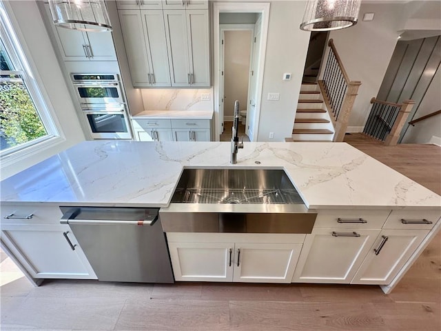 kitchen featuring light stone counters, white cabinetry, stainless steel appliances, pendant lighting, and a sink