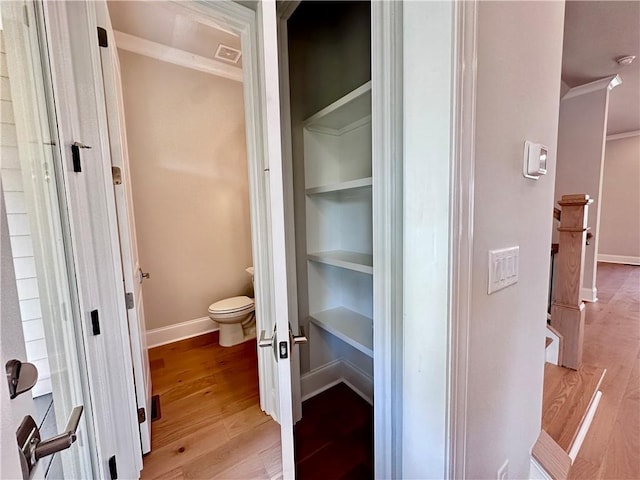 interior space featuring toilet, crown molding, wood finished floors, and baseboards