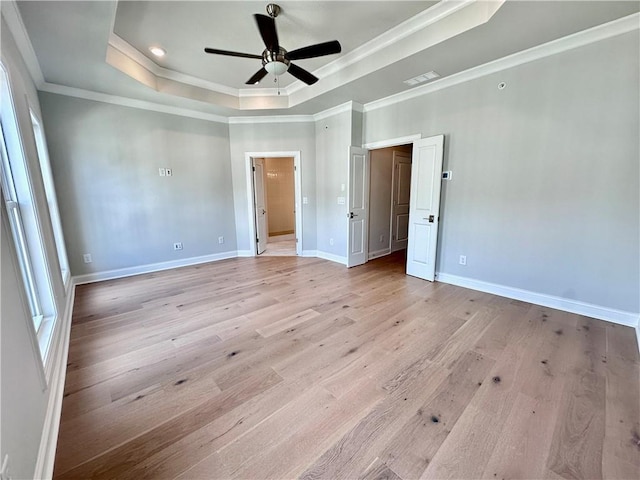 unfurnished bedroom featuring visible vents, baseboards, light wood-style floors, crown molding, and a tray ceiling