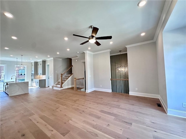 unfurnished living room with ceiling fan with notable chandelier, ornamental molding, visible vents, a sink, and baseboards