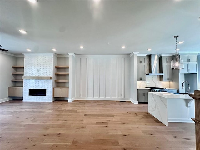 kitchen with crown molding, light wood-type flooring, wall chimney range hood, a sink, and gray cabinetry