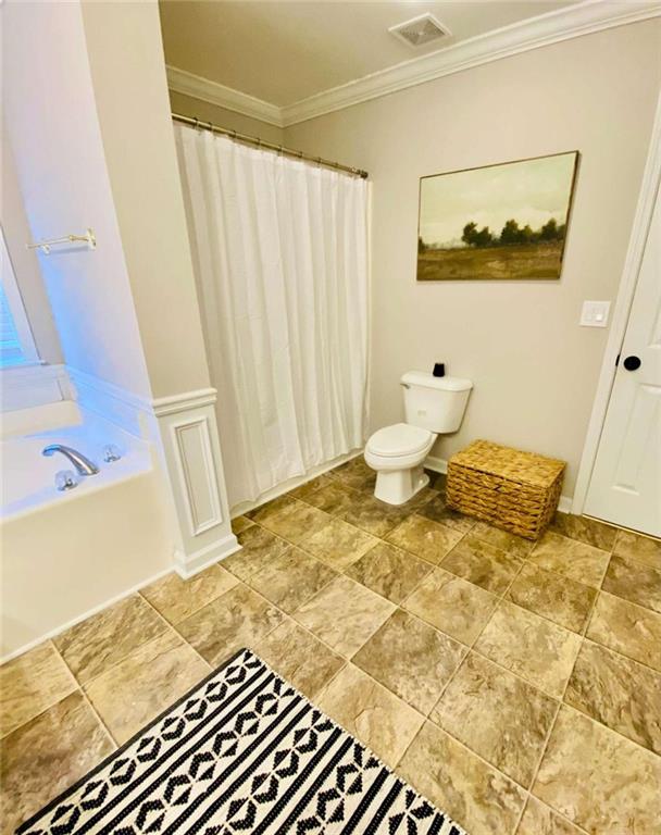 bathroom featuring ornamental molding, toilet, and a tub to relax in