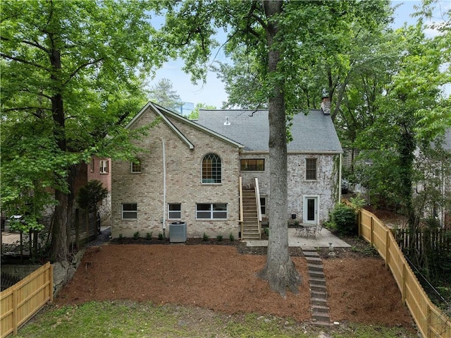 rear view of house featuring a patio area, stairway, a fenced backyard, brick siding, and a chimney