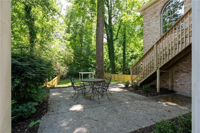 view of patio with fence, outdoor dining space, and stairs