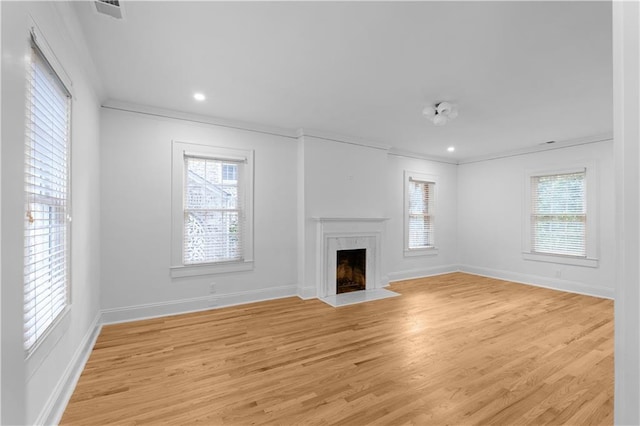 unfurnished living room with ornamental molding, plenty of natural light, a high end fireplace, light wood finished floors, and baseboards