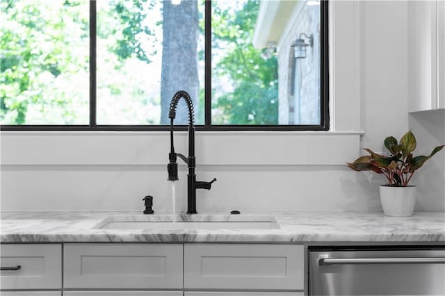 detailed view of a sink, stainless steel dishwasher, white cabinets, and light stone countertops