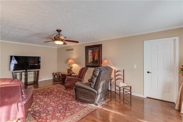 living room with hardwood / wood-style flooring, ornamental molding, ceiling fan, and a textured ceiling