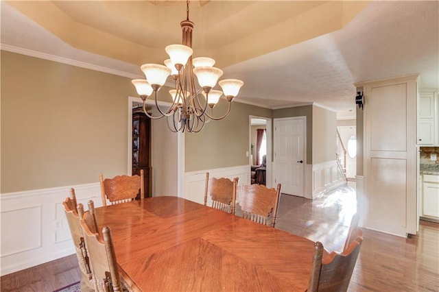 dining area with crown molding, a tray ceiling, a chandelier, and hardwood / wood-style floors