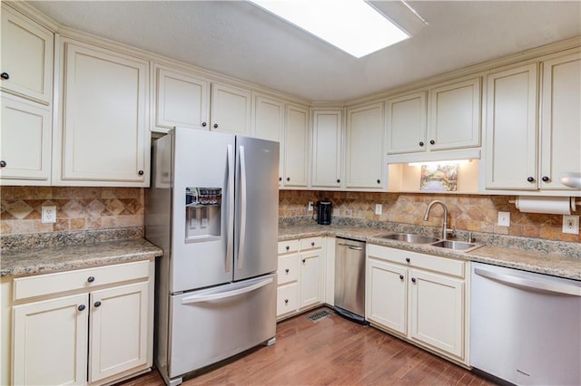 kitchen featuring stainless steel appliances, sink, decorative backsplash, and light hardwood / wood-style flooring