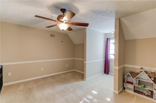 additional living space with vaulted ceiling, light colored carpet, ceiling fan, and a textured ceiling