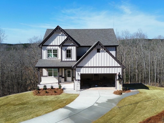 modern farmhouse with board and batten siding, roof with shingles, a front yard, a view of trees, and driveway