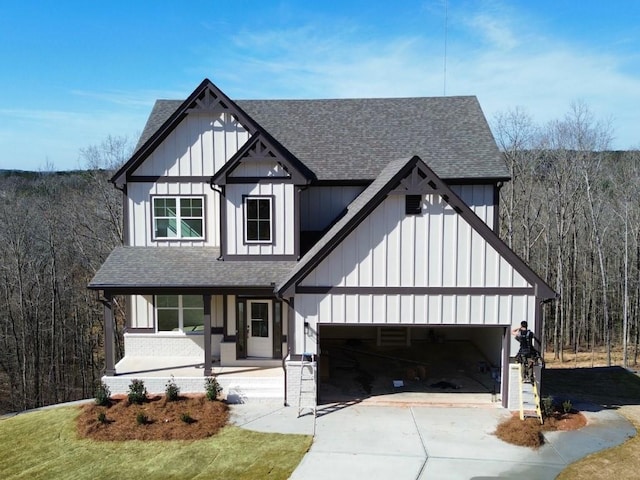 modern inspired farmhouse featuring a wooded view, driveway, roof with shingles, and board and batten siding