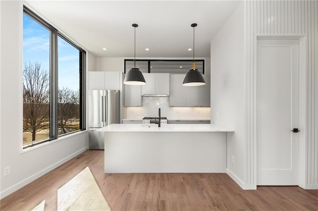 kitchen featuring decorative light fixtures, stainless steel fridge, white cabinets, and light wood-type flooring