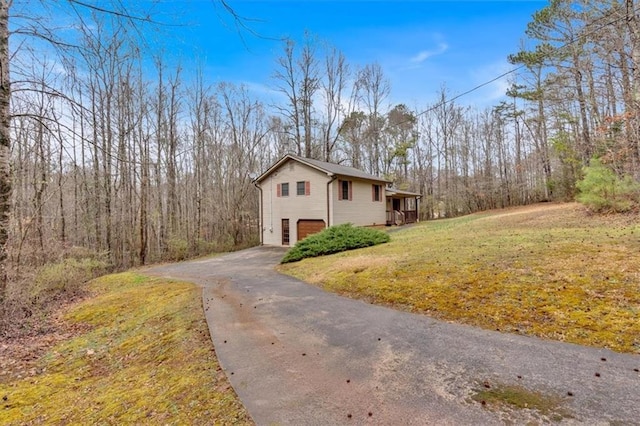 view of home's exterior featuring a garage, a lawn, a wooded view, and driveway