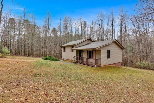 view of side of property featuring covered porch, a lawn, and a forest view