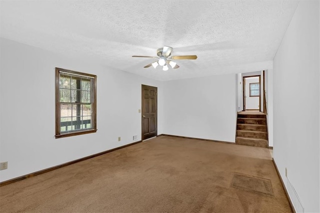 carpeted spare room featuring stairs, ceiling fan, baseboards, and a textured ceiling