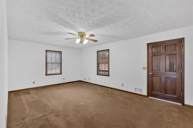 carpeted spare room with visible vents, a textured ceiling, a ceiling fan, and baseboards