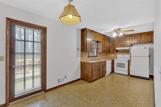 kitchen featuring visible vents, baseboards, under cabinet range hood, light countertops, and white appliances