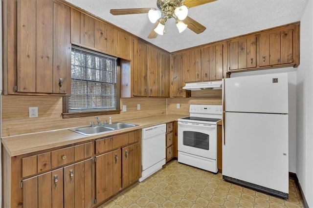 kitchen featuring under cabinet range hood, light floors, light countertops, white appliances, and a sink