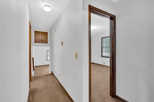 corridor with visible vents, light colored carpet, a textured ceiling, and baseboards