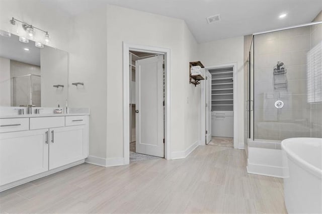 full bathroom with vanity, visible vents, a freestanding bath, a shower stall, and a walk in closet