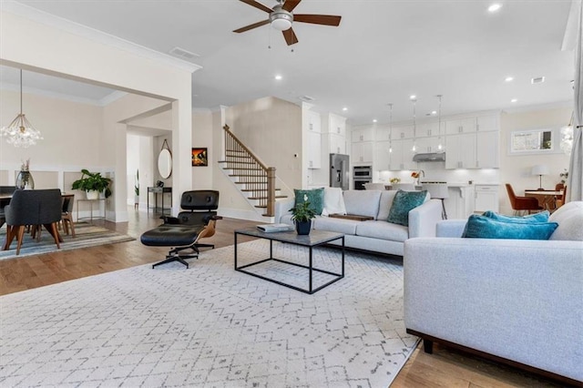 living area with recessed lighting, light wood-style floors, ornamental molding, and stairs