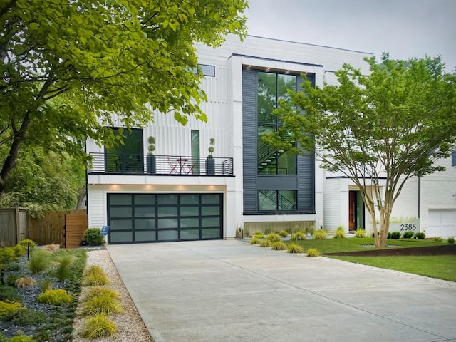 view of front of house featuring a balcony, concrete driveway, an attached garage, and fence