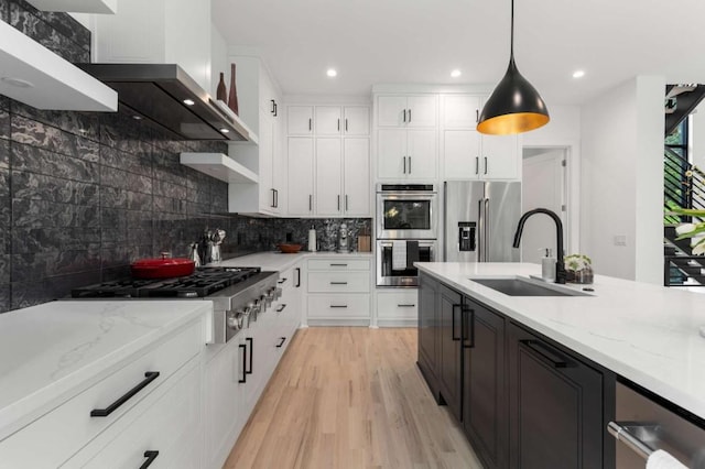 kitchen with a sink, stainless steel appliances, light wood-style flooring, decorative backsplash, and pendant lighting