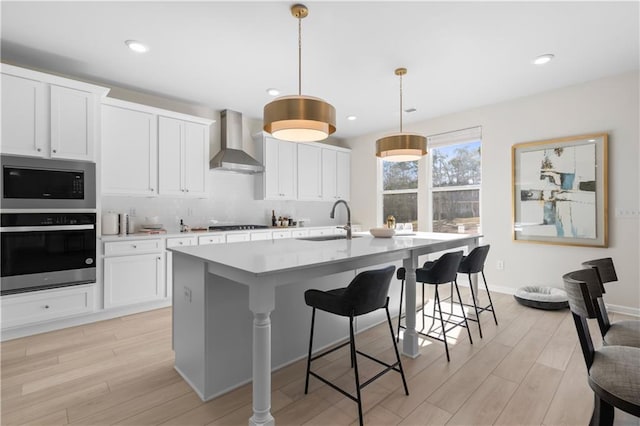 209 Chiswick Loop, Stockbridge, GA 30281 - kitchen with stainless steel appliances, wall chimney exhaust hood, light wood-style floors, a kitchen island with sink, and a breakfast bar