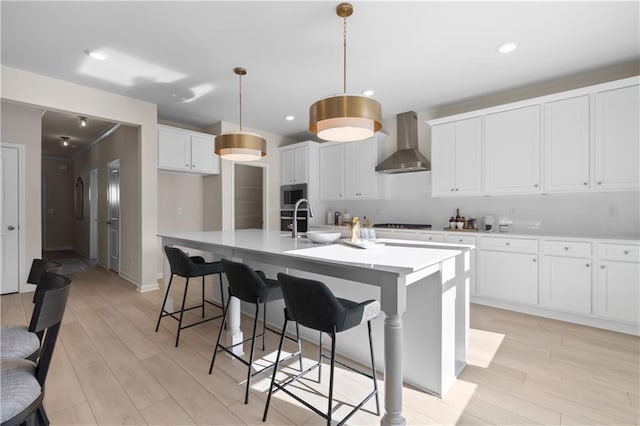209 Chiswick Loop, Stockbridge, GA 30281 - kitchen featuring wall chimney range hood, stainless steel microwave, a center island with sink, light countertops, and light wood-type flooring