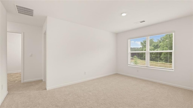 empty room with baseboards, visible vents, and light colored carpet