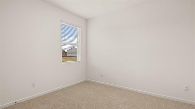 spare room featuring light colored carpet and baseboards