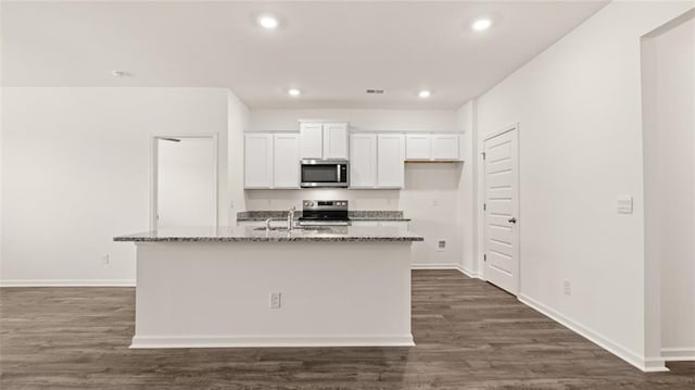 kitchen with dark stone countertops, a kitchen island with sink, white cabinets, and stainless steel appliances