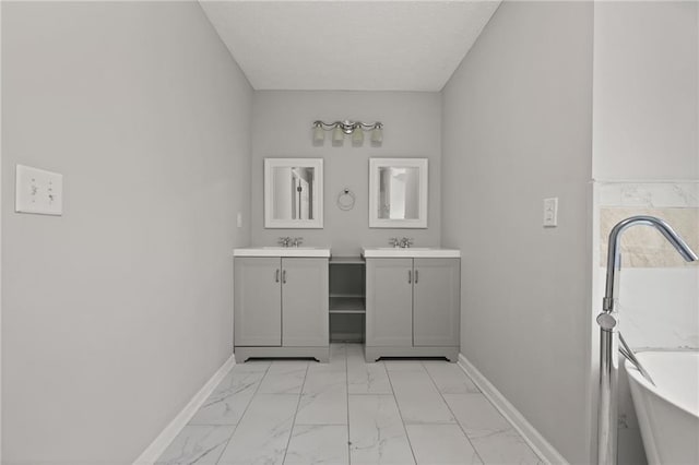 bathroom featuring two vanities, marble finish floor, a sink, baseboards, and a freestanding bath