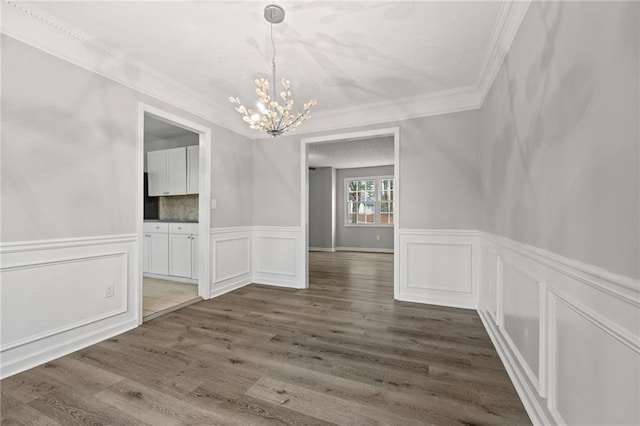 unfurnished dining area featuring crown molding, wood finished floors, wainscoting, and a chandelier