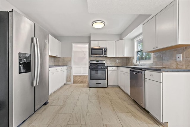 kitchen with a sink, stainless steel appliances, white cabinetry, dark countertops, and backsplash