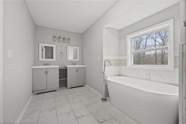 full bathroom featuring two vanities, baseboards, marble finish floor, and a textured ceiling