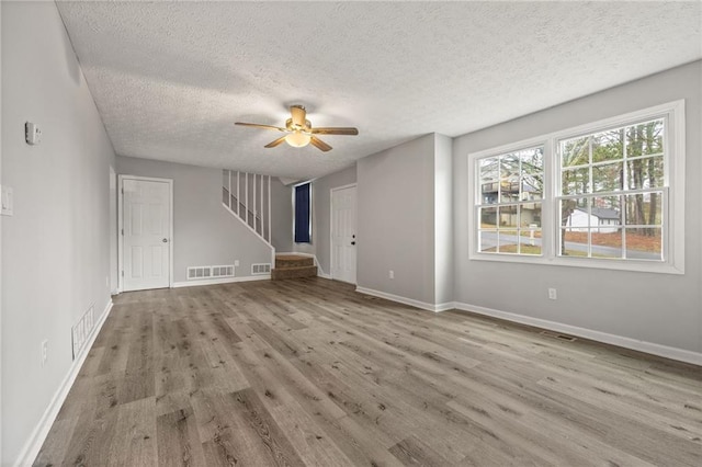 unfurnished living room with ceiling fan, stairway, visible vents, and wood finished floors