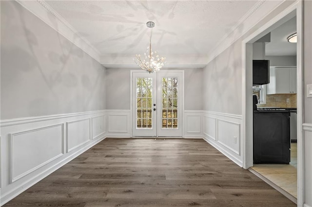 unfurnished dining area featuring crown molding, dark wood finished floors, wainscoting, french doors, and an inviting chandelier