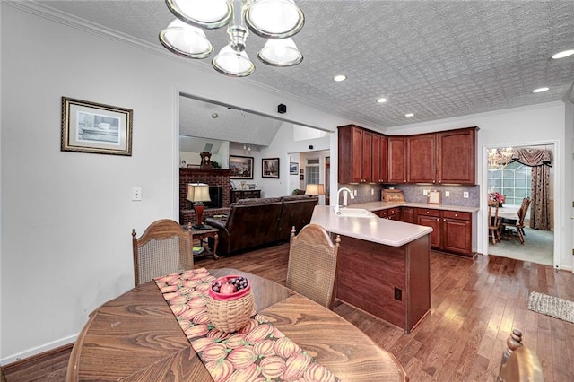 kitchen with an inviting chandelier, dark wood-type flooring, a brick fireplace, sink, and kitchen peninsula