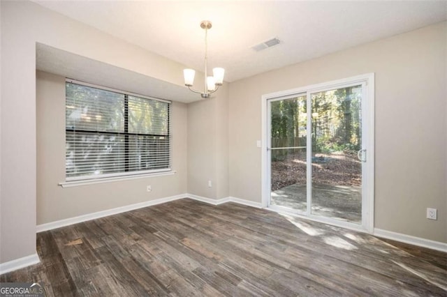 empty room with wood finished floors, a chandelier, and baseboards