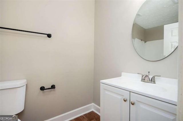 half bath with vanity, toilet, baseboards, and wood finished floors