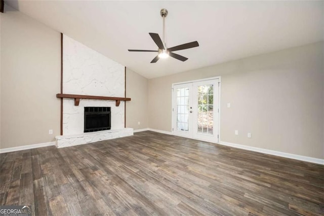 unfurnished living room with vaulted ceiling, a ceiling fan, wood finished floors, a stone fireplace, and baseboards